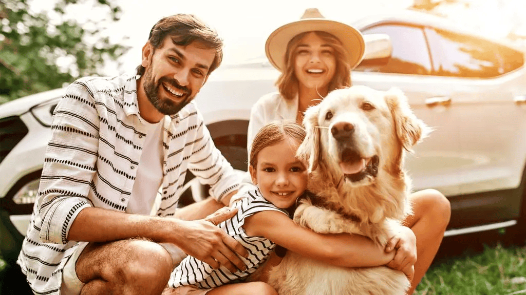 Family photo showing parents with a child and a dog in front of a car